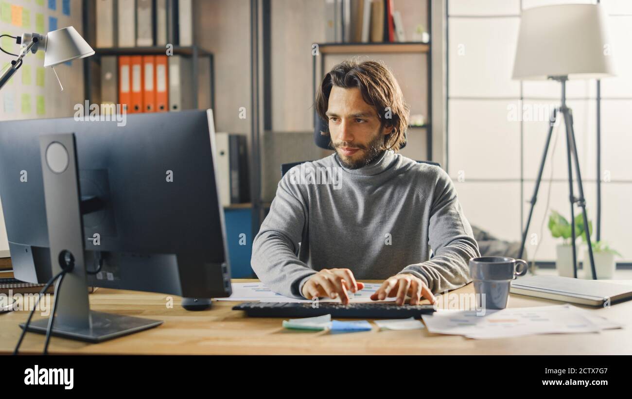 Creative Entrepreneur sitzt an seinem Schreibtisch arbeitet auf Desktop-Computer im stilvollen Büro. Handsome langhaarige hispanischen Mann mit künstlerischen Look verwendet Stockfoto