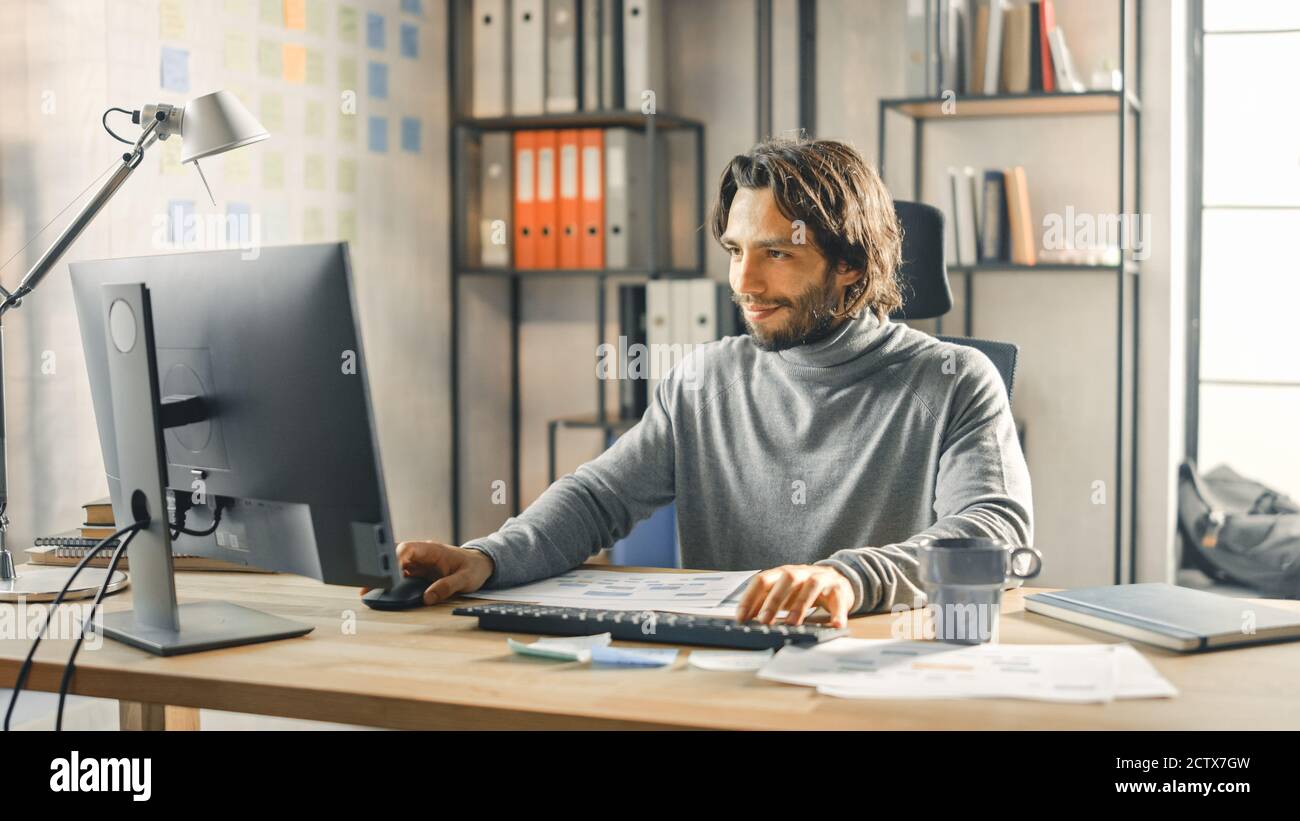 Creative Entrepreneur sitzt an seinem Schreibtisch arbeitet auf Desktop-Computer im stilvollen Büro. Handsome langhaarige hispanischen Mann mit künstlerischen Look verwendet Stockfoto