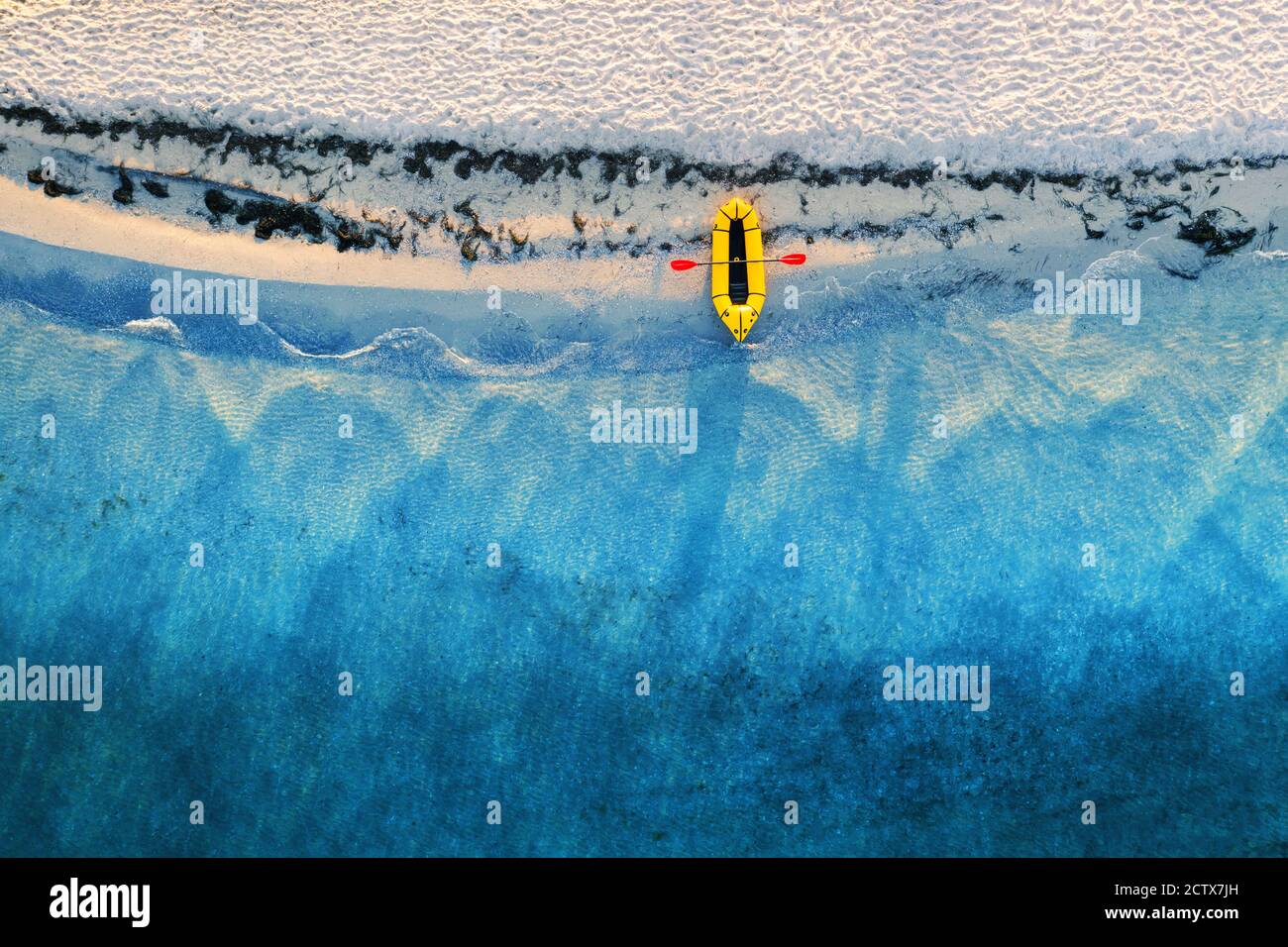 Gelbes Packfloß Gummiboot mit roter Pfanne und türkisfarbenen Wasserwellen von oben. Strand mit gelbem Sand, der vom Sonnenlicht leuchtet. Reise Sommer Ferien Seesapfel Hintergrund von Drohne Stockfoto