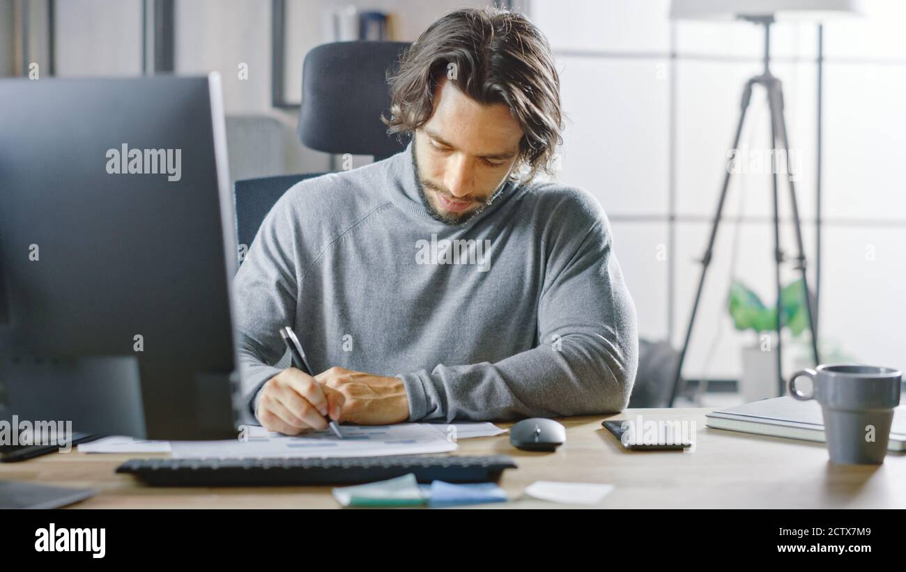 Schöner langhaariger Unternehmer sitzt an seinem Schreibtisch im Büro arbeitet auf Desktop-Computer, arbeiten mit Dokumenten, Charts, Grafiken, Statistik und Stockfoto