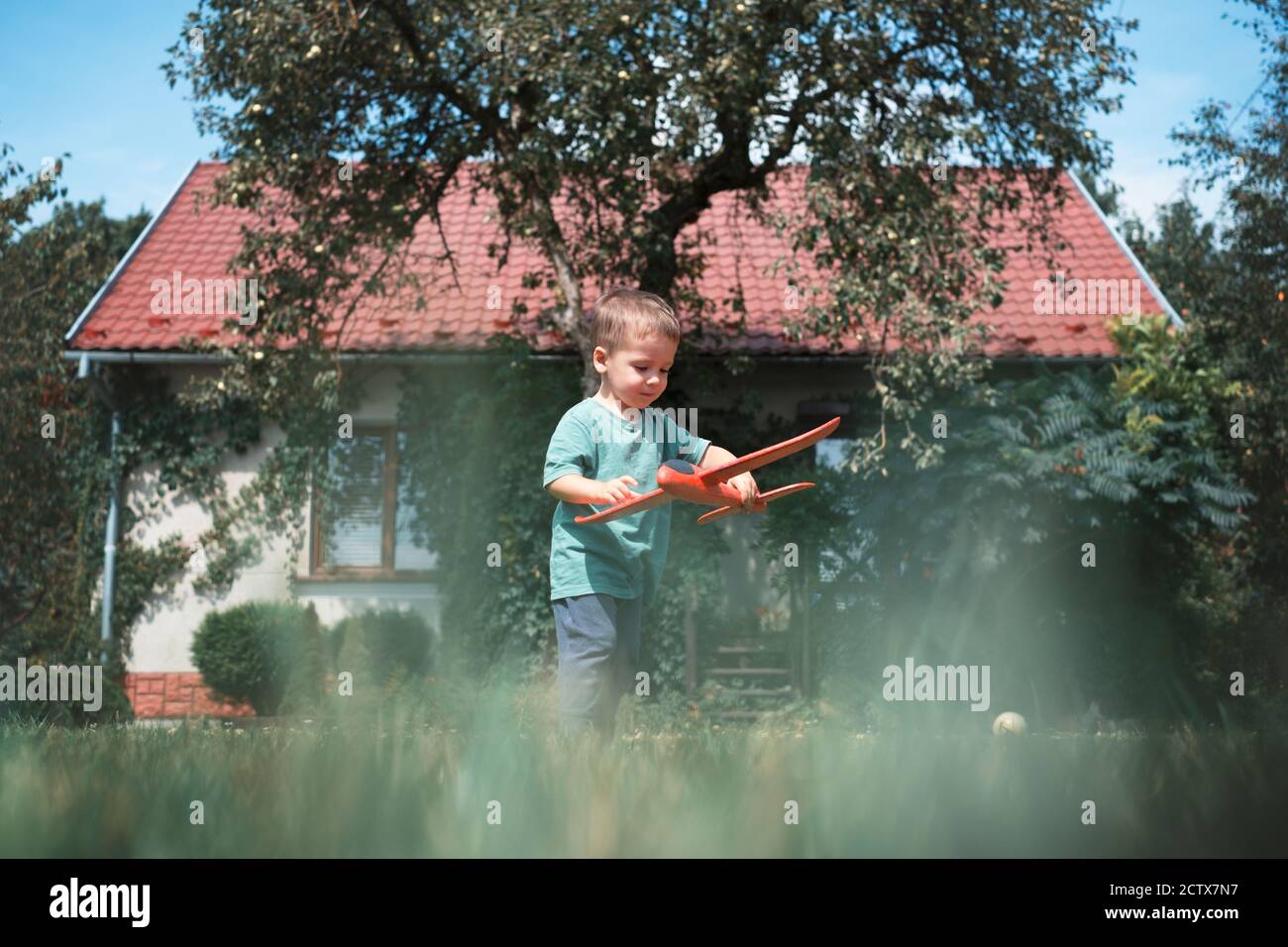 Glückliches Kind spielt mit roten Flugzeug auf Rasen in der Nähe seiner Zu Hause Stockfoto