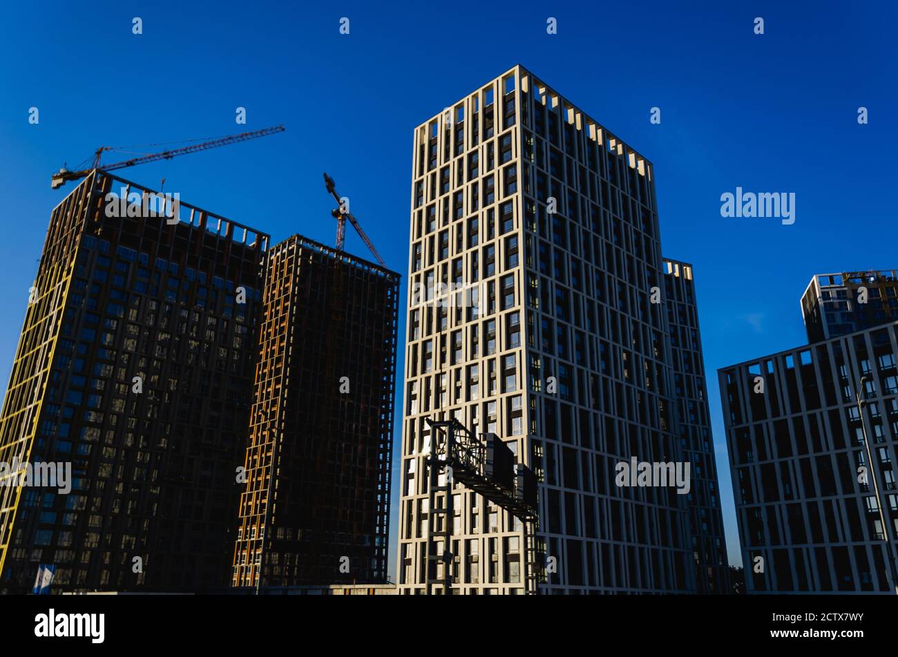 Wohnungsentwicklung. Moderne Hochhäuser im Bau und Kräne vor dem klaren blauen Himmel. Städtischer Hintergrund. Konzept der Zersiedelung Stockfoto