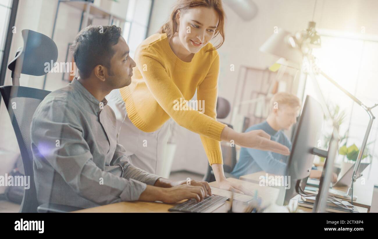 Handsome Indian Professional sitzt an seinem Schreibtisch Arbeiten auf Laptop-Computer, Young Beautiful Team Leader gibt Ratschläge über Projekt-Details. Büro Stockfoto