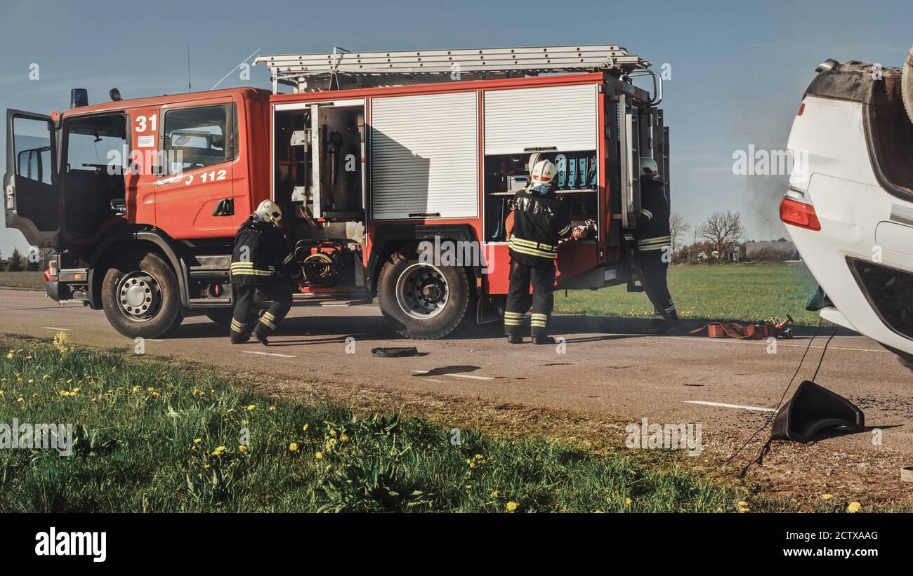 Feuerwehrleute kommen auf der Auto Crash Traffic Accident Szene auf ihrer Feuerwehrmaschine. Feuerwehrleute greifen ihre Werkzeuge, Ausrüstung und Ausrüstung von Fire Truck, Rush Stockfoto