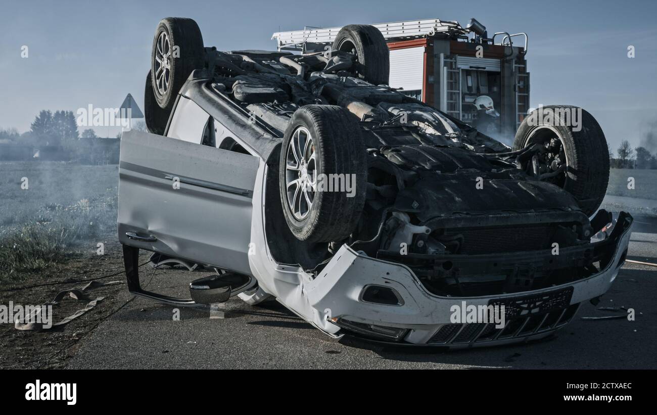 Horrific Verkehrsunfall Rollover Rauchen und brennendes Fahrzeug auf seinem Dach in der Mitte der Straße nach Kollision liegen. Im Hintergrundteam von Stockfoto