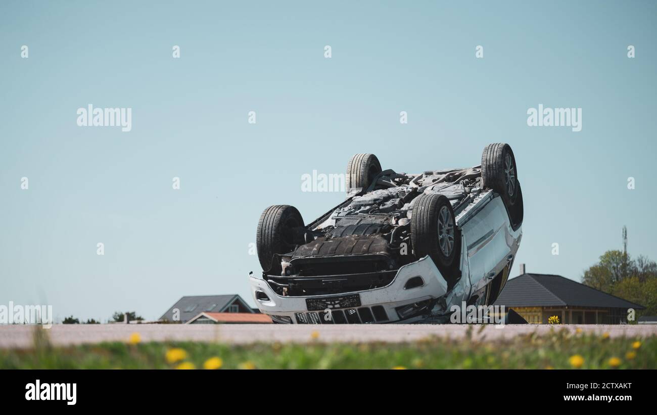 Horrific Verkehrsunfall Rollover Rauchen und brennendes Fahrzeug auf seinem Dach in der Mitte der Straße nach Kollision liegen. Crash-Szene tagsüber mit Stockfoto