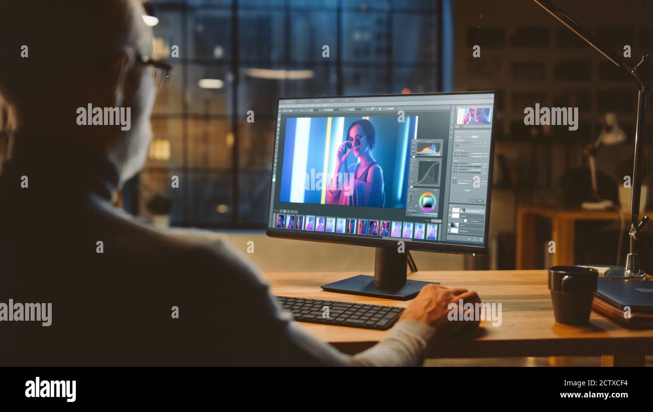 Über die Schulter: Creative Middle Aged Digital Editor arbeitet in Photo Editing Software auf seinem Personal Computer mit Big Display. Im Hintergrund Stockfoto