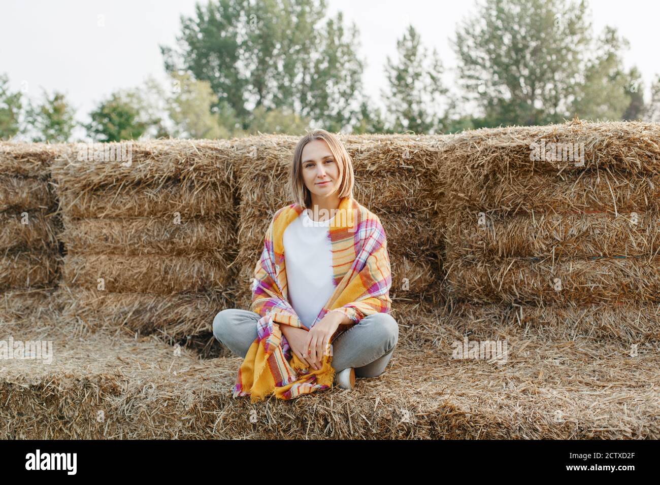 Herbst Herbst Frau Porträt. Portrait der schönen kaukasischen Frau mittleren Alters auf Heuhaufen auf dem Bauernhof sitzen. Nachdenkliche Frau in gelben Schal gewickelt Stockfoto
