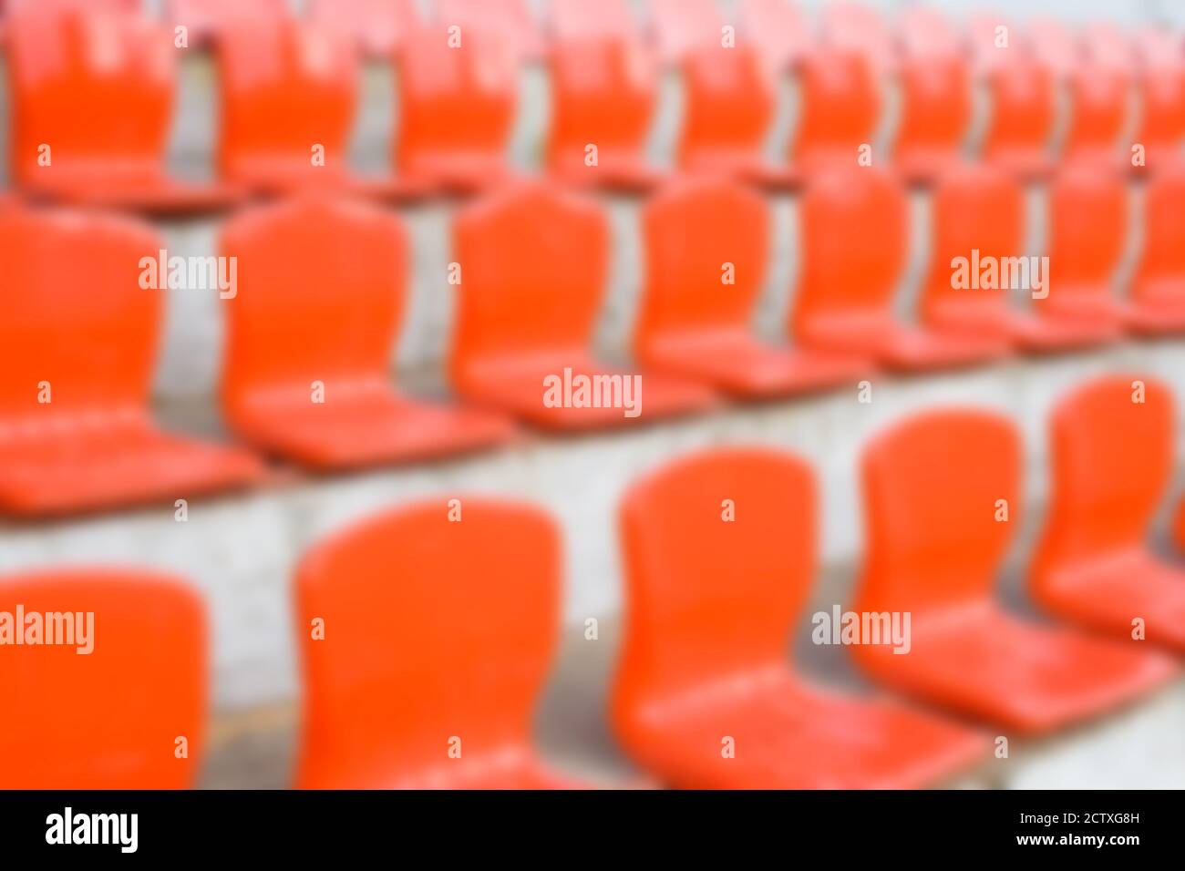 Verschwommene rote leere Plastiksitze eines kleinen Stadions. Hintergrund horizontal verwischen Stockfoto