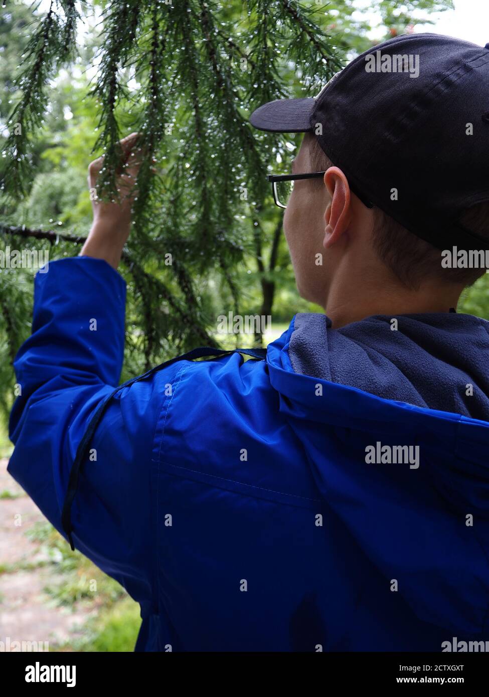 Ein junger Mann mit Brille Ich habe eine helle Jacke neben einem Baum. Stockfoto
