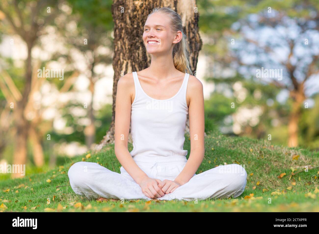 Glückliche junge Frau, die auf dem Gras im Park sitzt. Wohlbefinden und gesundes Leben. Stockfoto