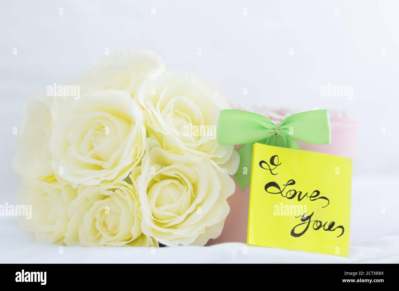 Romantisches Geschenk. Blumenstrauß aus weißen Rosen, Geschenkbox und 'I Love You'-Notiz auf einem Bett. Nahaufnahme. Stockfoto