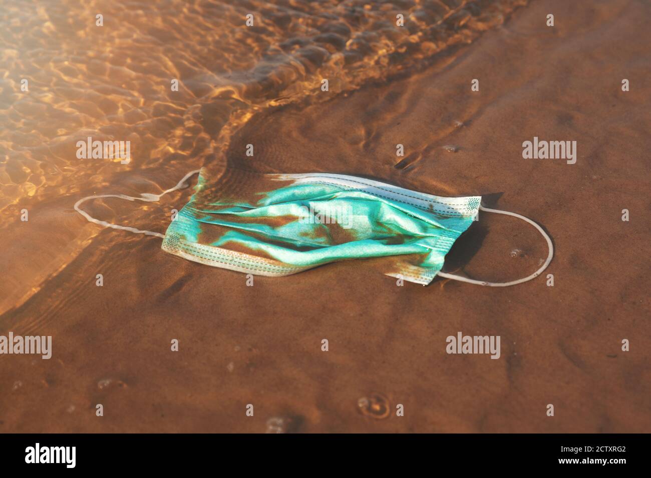 Infektiöse Abfälle - medizinische Gesichtsmaske im Wasser auf dem Strand Sand. Meer und Meeresverschmutzung seit covid-19 Stockfoto