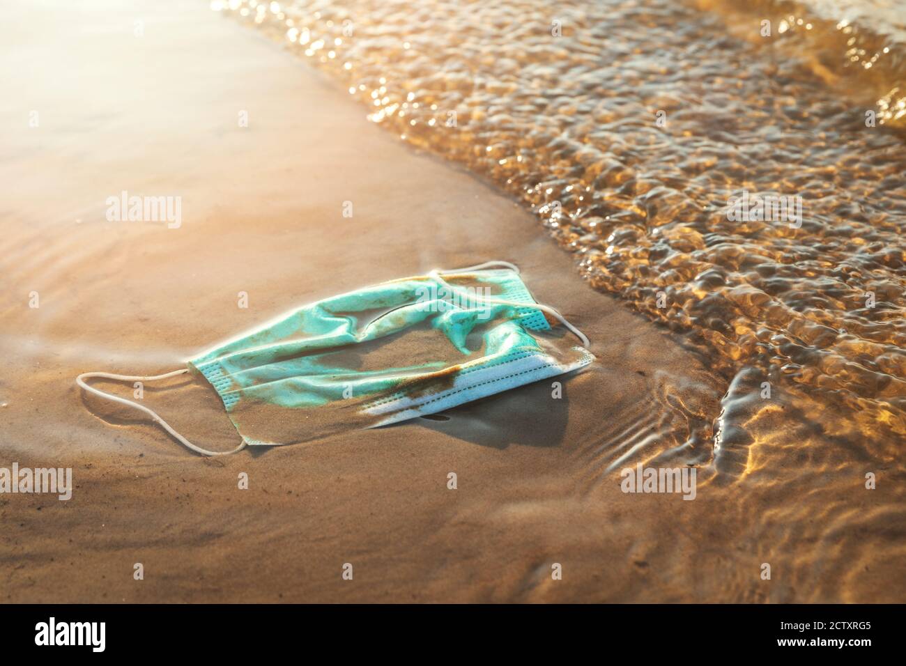 Medizinische Abfälle - Schutzmaske im Wasser an der Strandküste Sand. Meer und Meeresverschmutzung Stockfoto