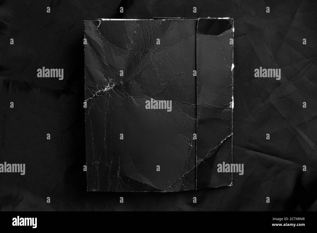 Schwarzes zerknittertes Papier mit ausgefransten Falten auf schwarzem zerknittertem Kunstmaterial. Nahaufnahme. Grunge-Modell. Speicherplatz kopieren. Stockfoto
