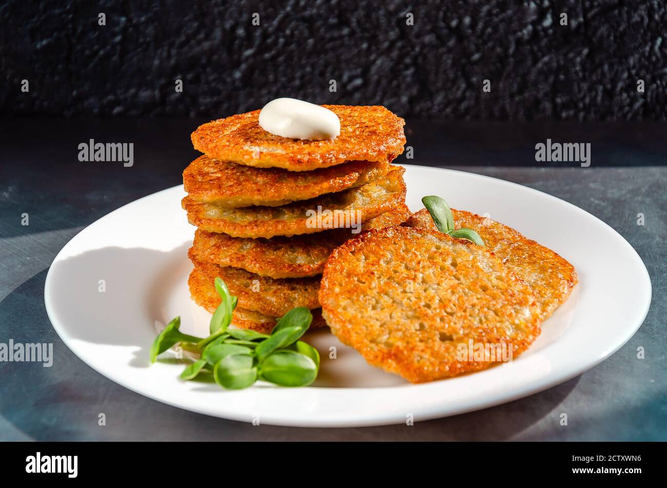 Hausgemachte Kartoffelpfannkuchen, Latkes, Draniki, Rösti oder Krapfen serviert mit Sauerrahm und Sonnenblumensprossen. Traditionelle Hanukkah-Leckereien. Nahaufnahme Stockfoto