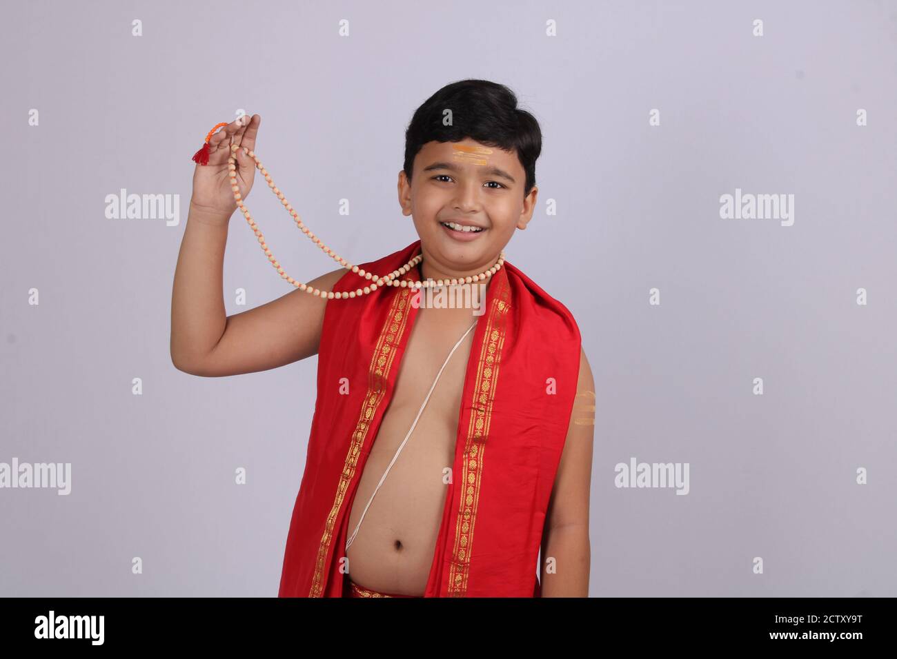 Indischer Junge in ethnischer Kleidung zeigt seinen Rosenkranz oder Kette von Gebetsperlen mit Lächeln. Stockfoto