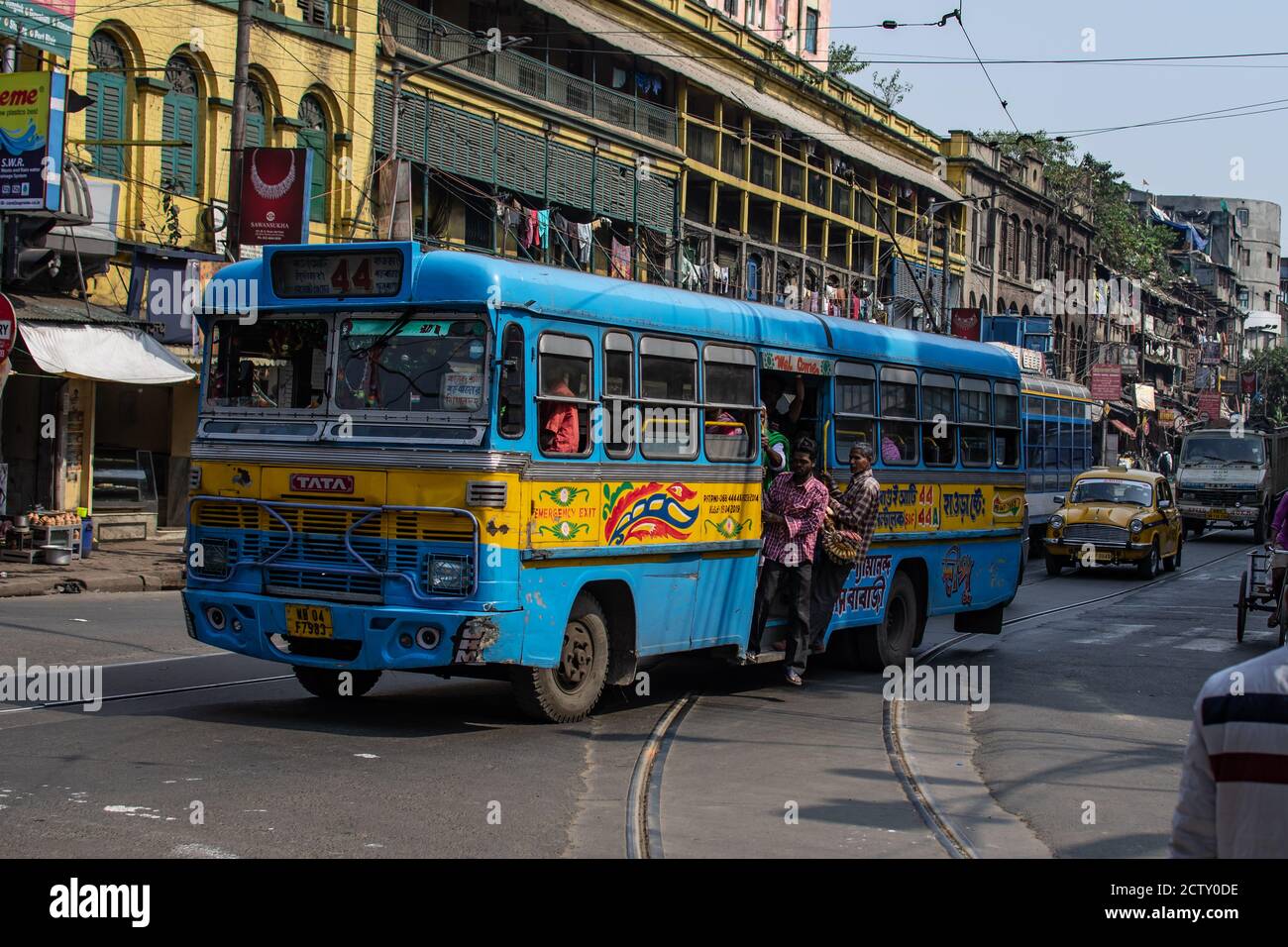 Kolkata, Indien - 2. Februar 2020: Ein blauer und gelber traditioneller öffentlicher Personenbus im Verkehr mit nicht identifizierten Fahrgästen vor einer Straßenbahn Stockfoto