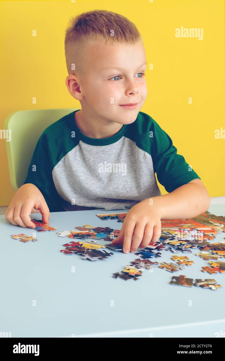 Portrait eines niedlichen Jungen, der am Tisch sitzt und Puzzles zusammenstellt. Frühzeitiges Lernen. Auf gelbem Hintergrund Stockfoto