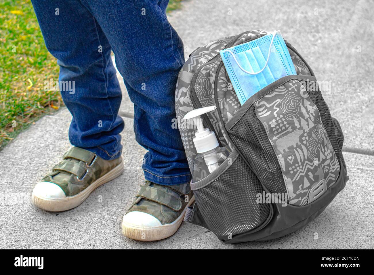 Kinderschuhe neben einer Schultasche mit einem Gesicht Maske und Handdesinfektionsmittel Stockfoto