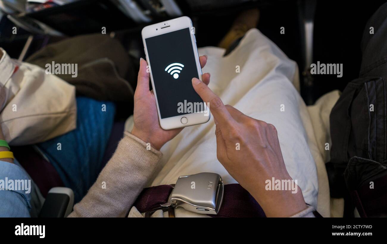 Asiatische Frau hält das Smartphone und erhalten die kostenlose WiFi in einem Flugzeug Reisen. Reisende setzen sich mit dem Telefon ins Flugzeug Stockfoto