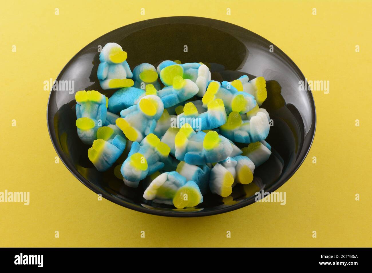 Sour Foam Fruit Gummy Candy in Form von Pinguinen in Schwarze Snack-Schale auf gelbem Hintergrund Stockfoto