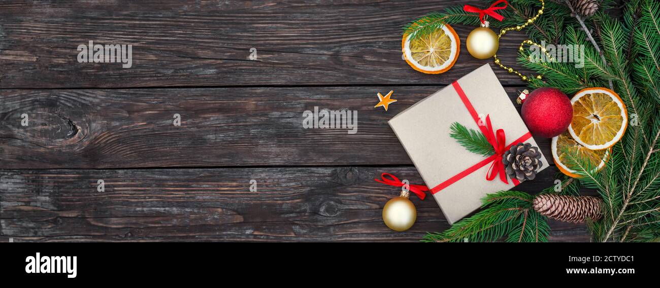Komposition zu Weihnachten oder Neujahr. Geschenkbox mit Tannenzweigen, Zapfen und Dekorationen auf einem rustikalen Holztisch als festlicher Hintergrund mit Kopierraum. Stockfoto