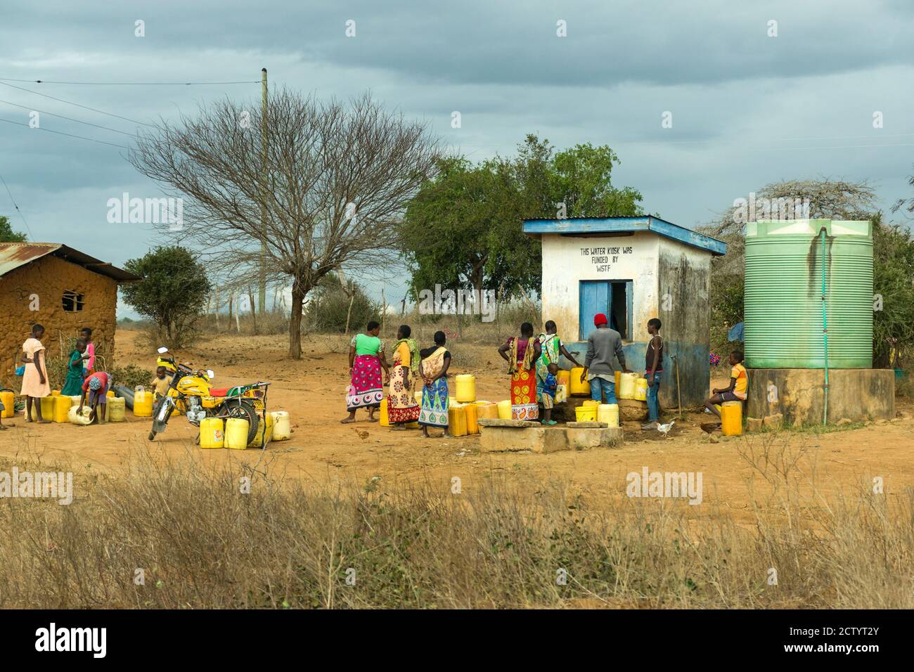 Eine Gruppe von afrikanischen Frauen und Kinder Schlange wasser Behälter an einem Wasser Kiosk im ländlichen Kenia zu füllen Stockfoto