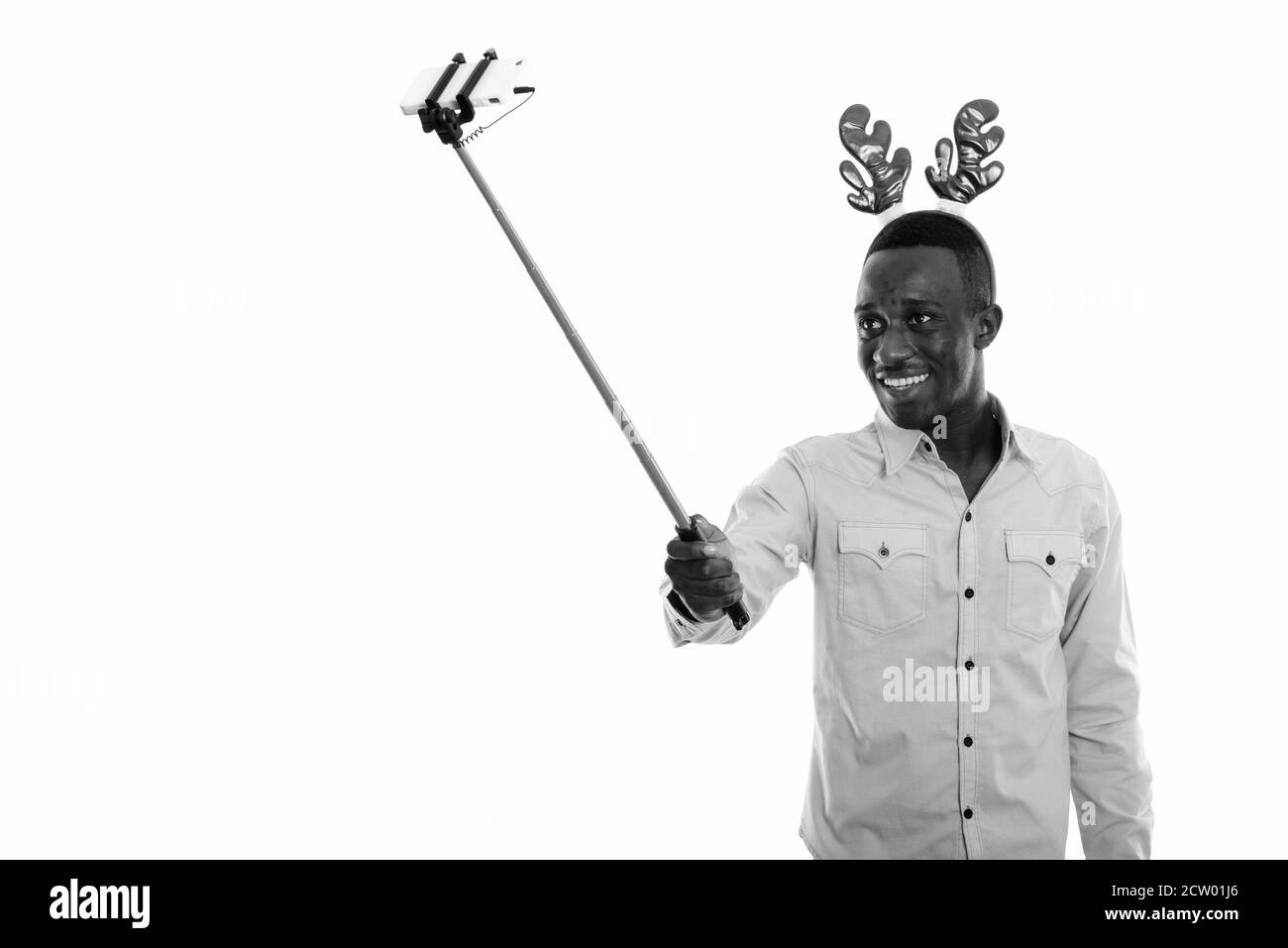 Glücklicher junger afrikanischer Mann mit Rentier-Stirnband während der Selfie-Aufnahme Mit Handy auf Selfie-Stick Stockfoto