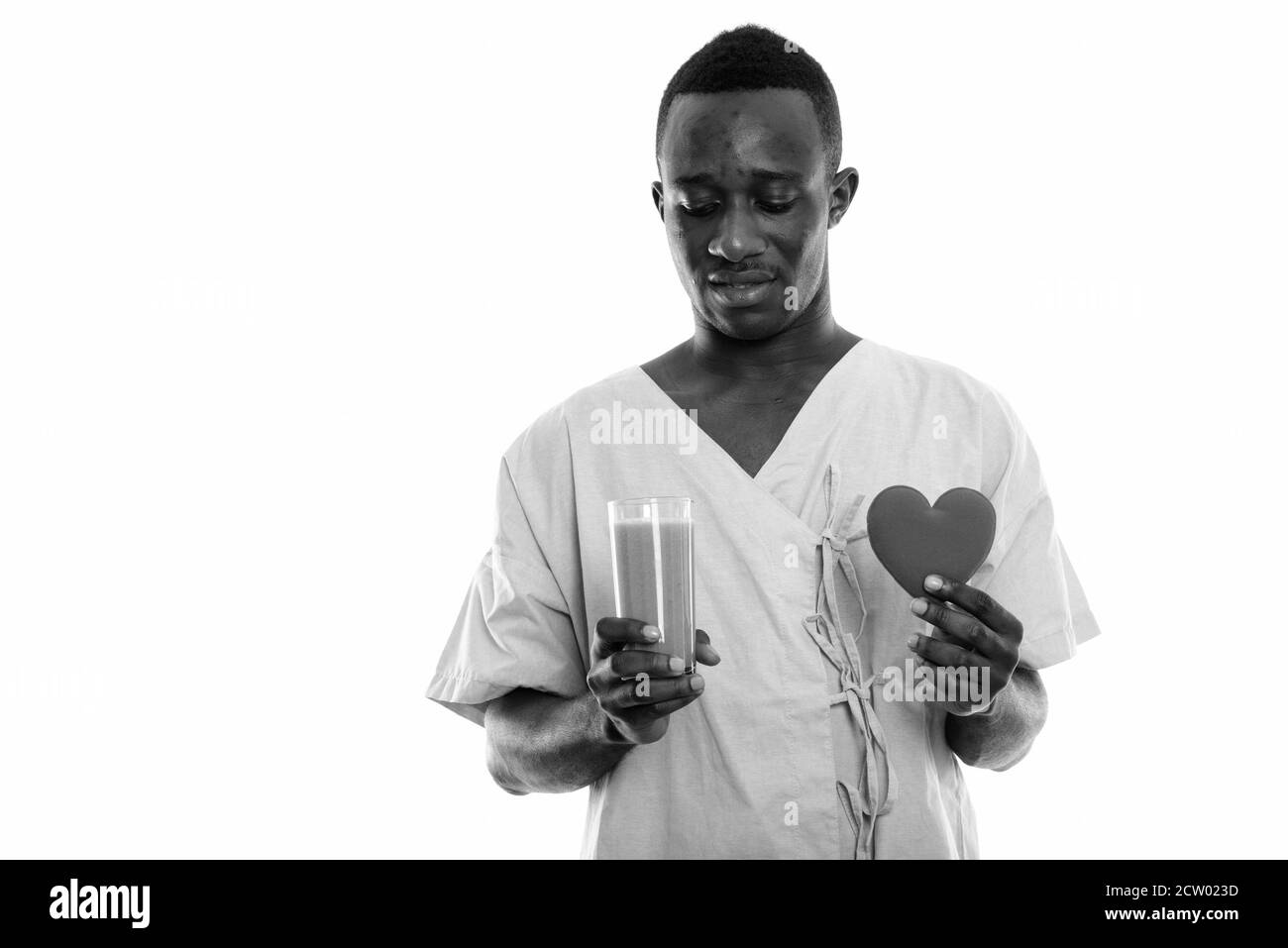 Studioaufnahme des jungen schwarzen afrikanischen Mannes Patienten beim Betrachen Glas Gemüsesmoothie und Herz halten Stockfoto