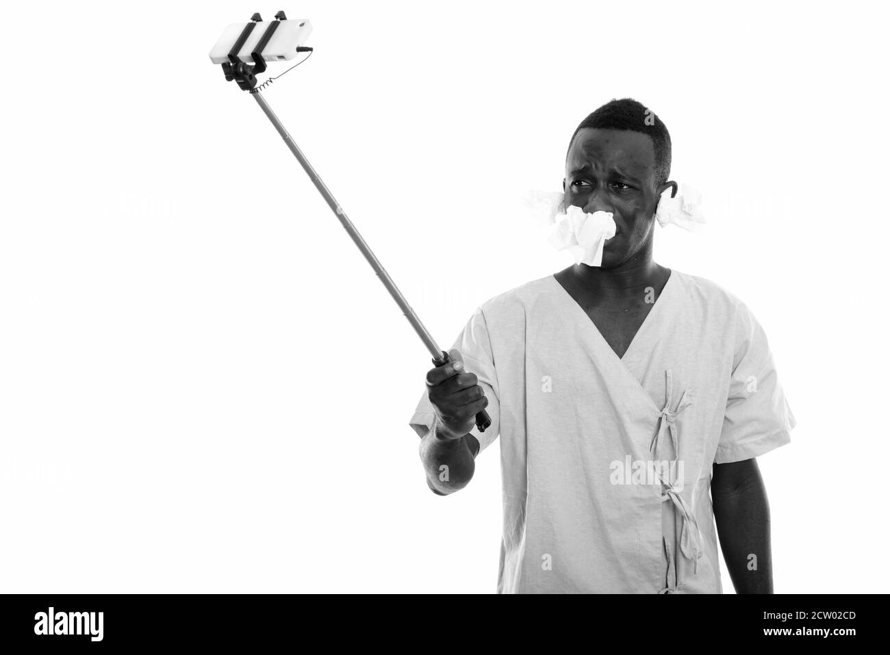 Junger afrikanischer Mann Patient nimmt Selfie-Bild mit Handy Auf Selfie Stick mit Taschentüchern an den Ohren und Nase Stockfoto Junger afrikanischer Mann Patient nimmt Selfie-Bild mit Handy Auf Selfie Stick mit Taschentüchern an den Ohren und Nase Stockfoto