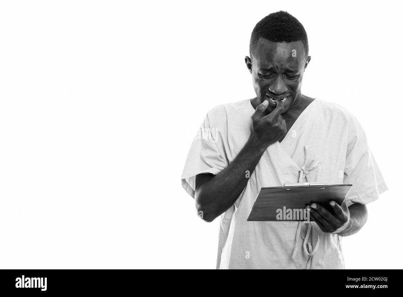 Studio shot von jungen schwarzen afrikanischen Mann Patienten auf Zwischenablage beim Suchen besorgt und Beißen seiner Fingernagel Stockfoto