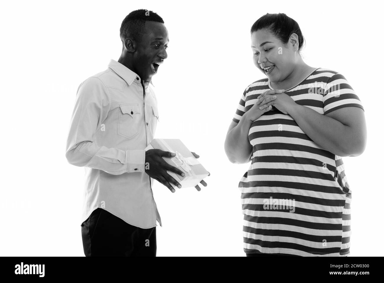 Gerne jungen schwarzen afrikanischen Mann, Geschenk, um junge Fett asiatische Frau lächelnd und überrascht Stockfoto