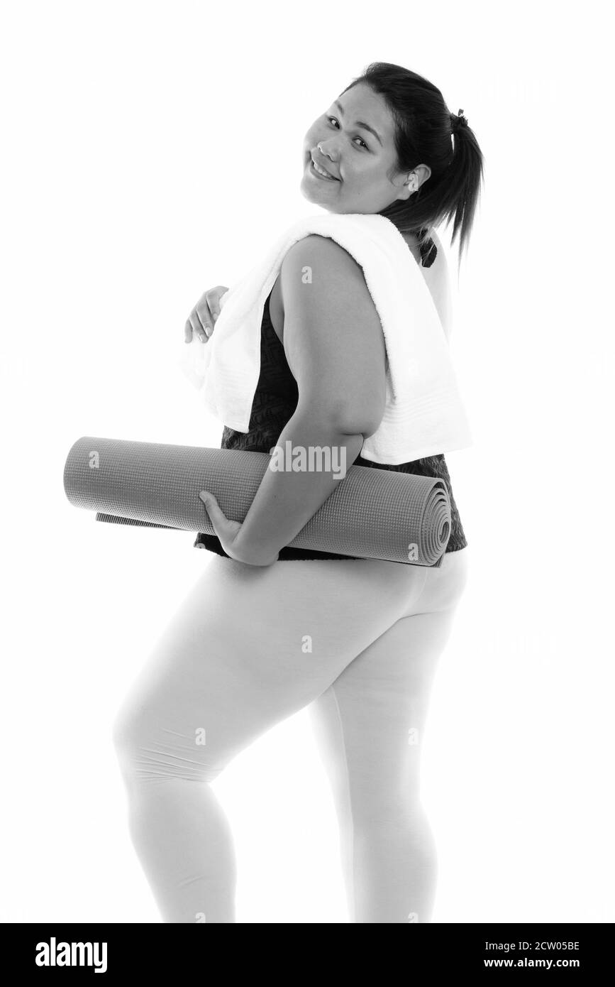 Studio shot der Jungen gerne Fett asiatische Frau lächelnd und sieht zurück halten Yoga Matte mit Handtuch über der Schulter Stockfoto