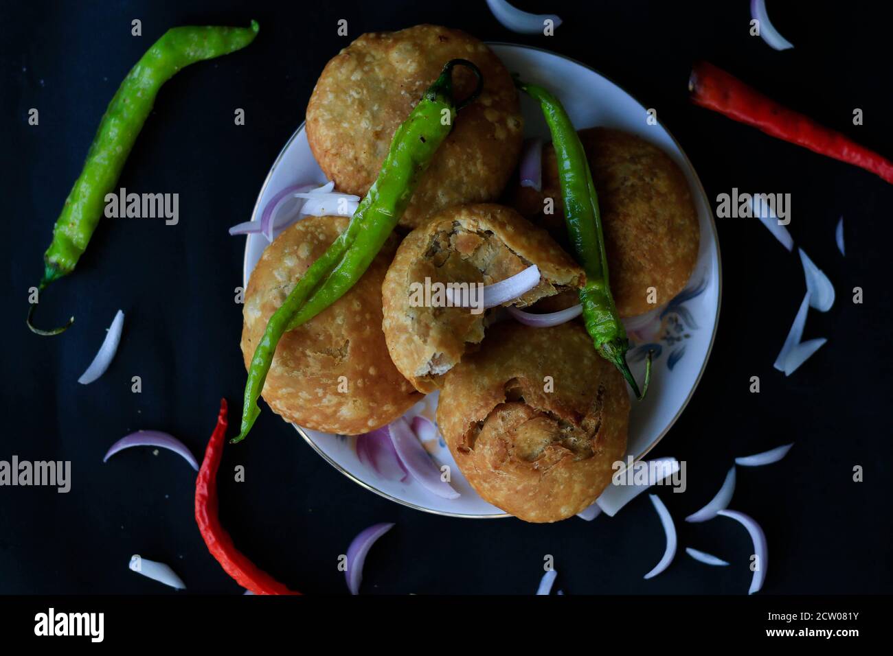 Leckere indische Snack Kachori aufeinander gestapelt und serviert mit grünen Chilis und Zwiebeln mit einem schwarzen Hintergrund aus dem oberen Winkel. Stockfoto