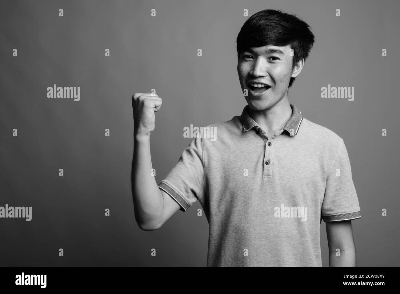Jungen asiatischen Mann, grau Poloshirt gegen grauer Hintergrund Stockfoto
