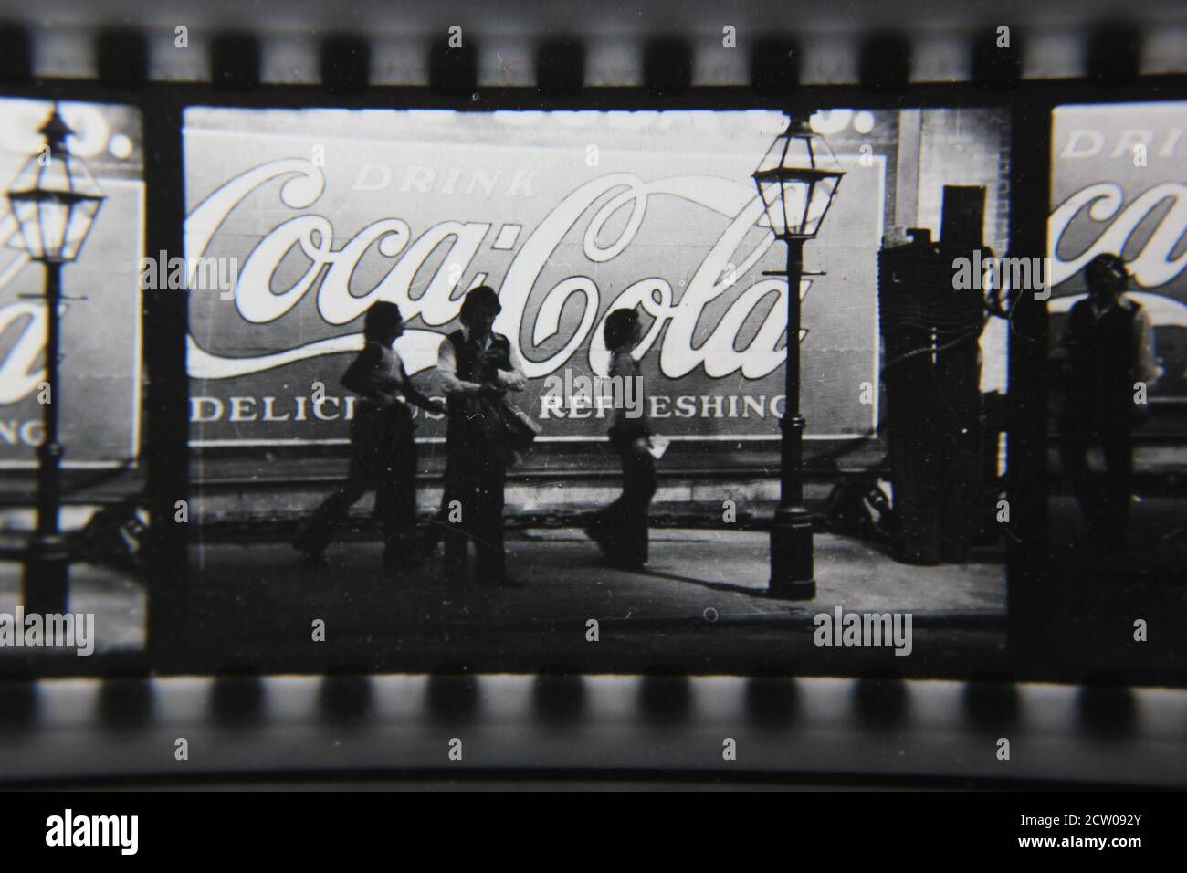 Feine Vintage-Schwarz-Weiß-Fotografie der 1970er Jahre von Profilen von Stadtmenschen, die vor einer riesigen Coca-Cola-Anzeige auf einer Wand gemalt gehen. Stockfoto