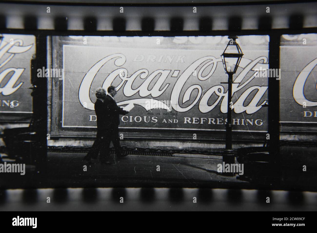 Feine Vintage-Schwarz-Weiß-Fotografie der 1970er Jahre von Profilen von Stadtmenschen, die vor einer riesigen Coca-Cola-Anzeige auf einer Wand gemalt gehen. Stockfoto