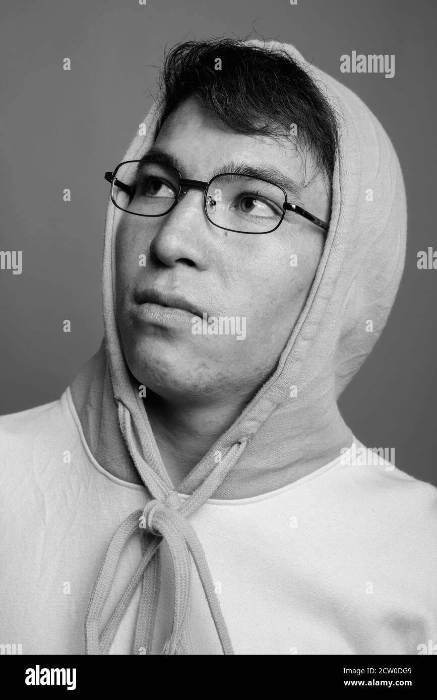 Junger asiatischer Mann mit buntem Kapuzenpullover und Brillen gegen Grau Hintergrund Stockfoto