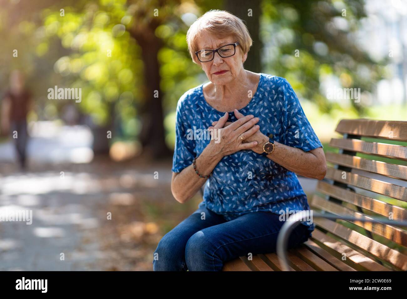 Ältere Frau, Die An Brustschmerzen Leidet, Während Sie Auf Der Bank Sitzt Stockfoto
