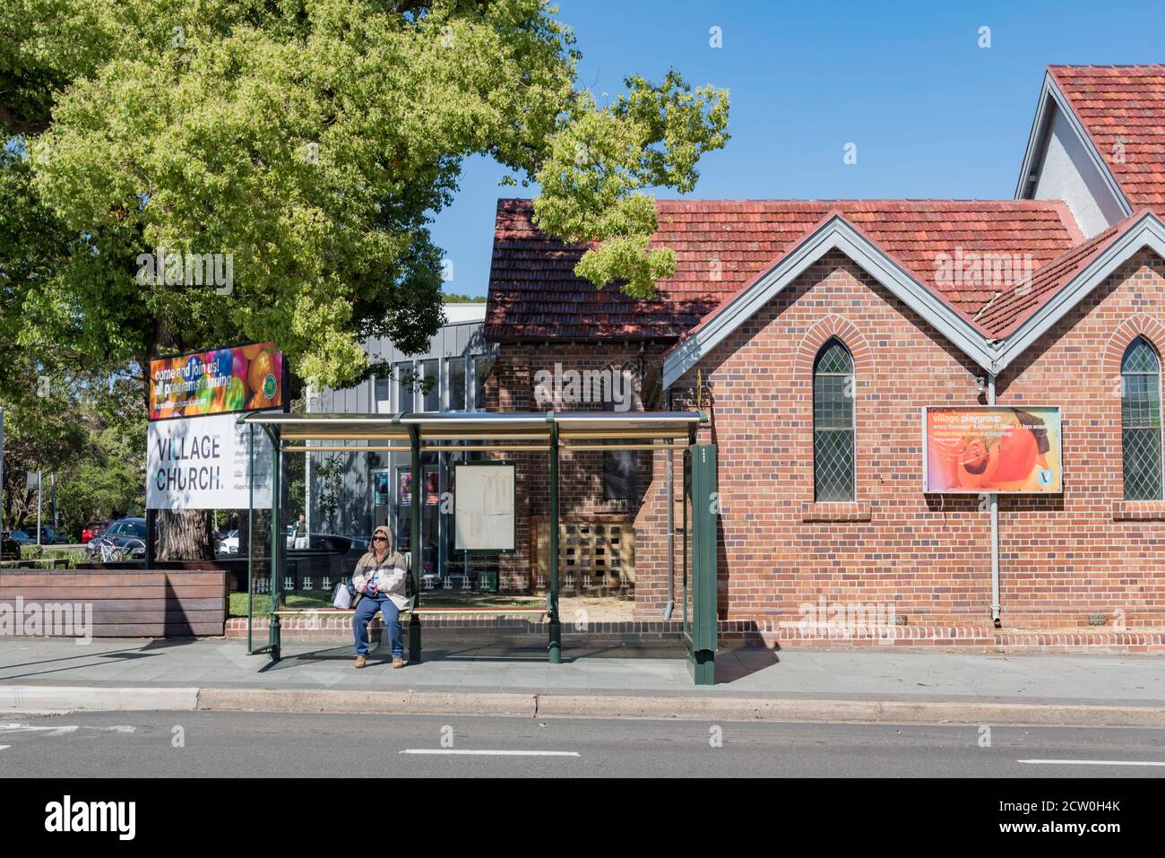 Eine Person sitzt an einer Bushaltestelle mit Glas- und Stahlrahmen in der Booth Street im Vorort Annandale in Sydney, Australien und wartet auf einen Bus Stockfoto