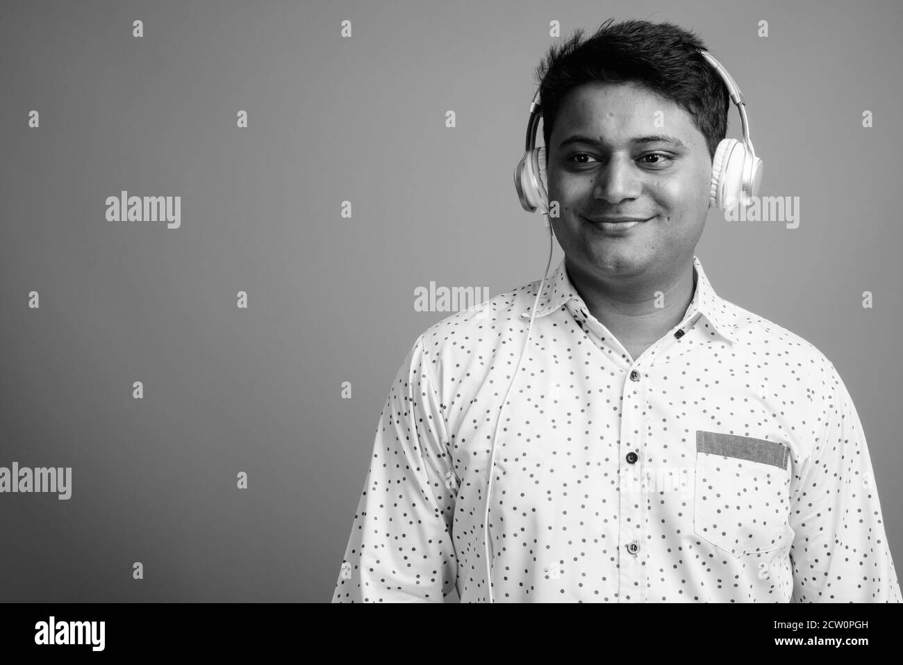 Junger indischer Geschäftsmann, der vor grauem Hintergrund Musik hört Stockfoto