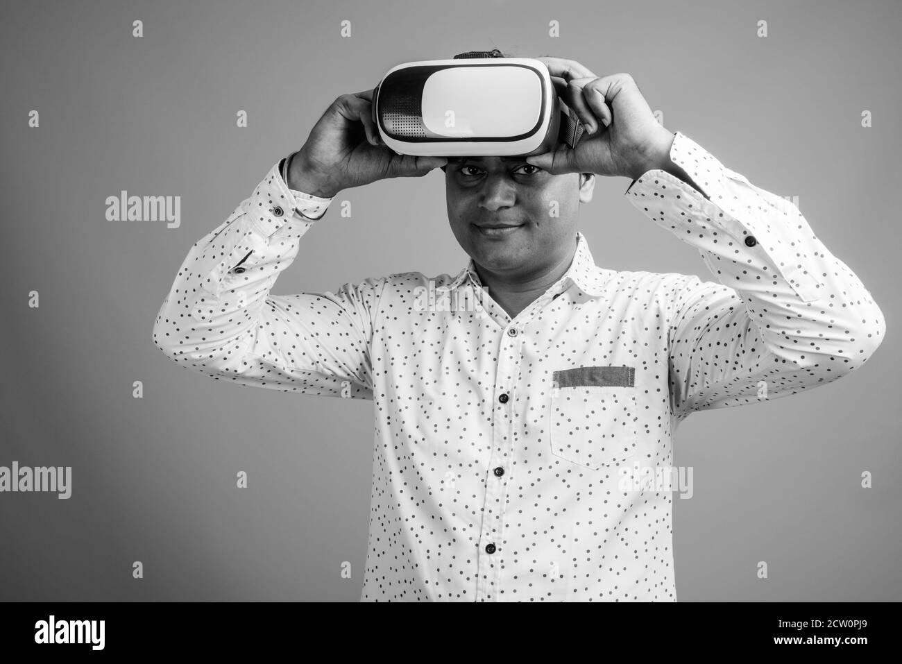 Junge indische Geschäftsmann mit Virtual Reality-Headset vor grauem Hintergrund Stockfoto