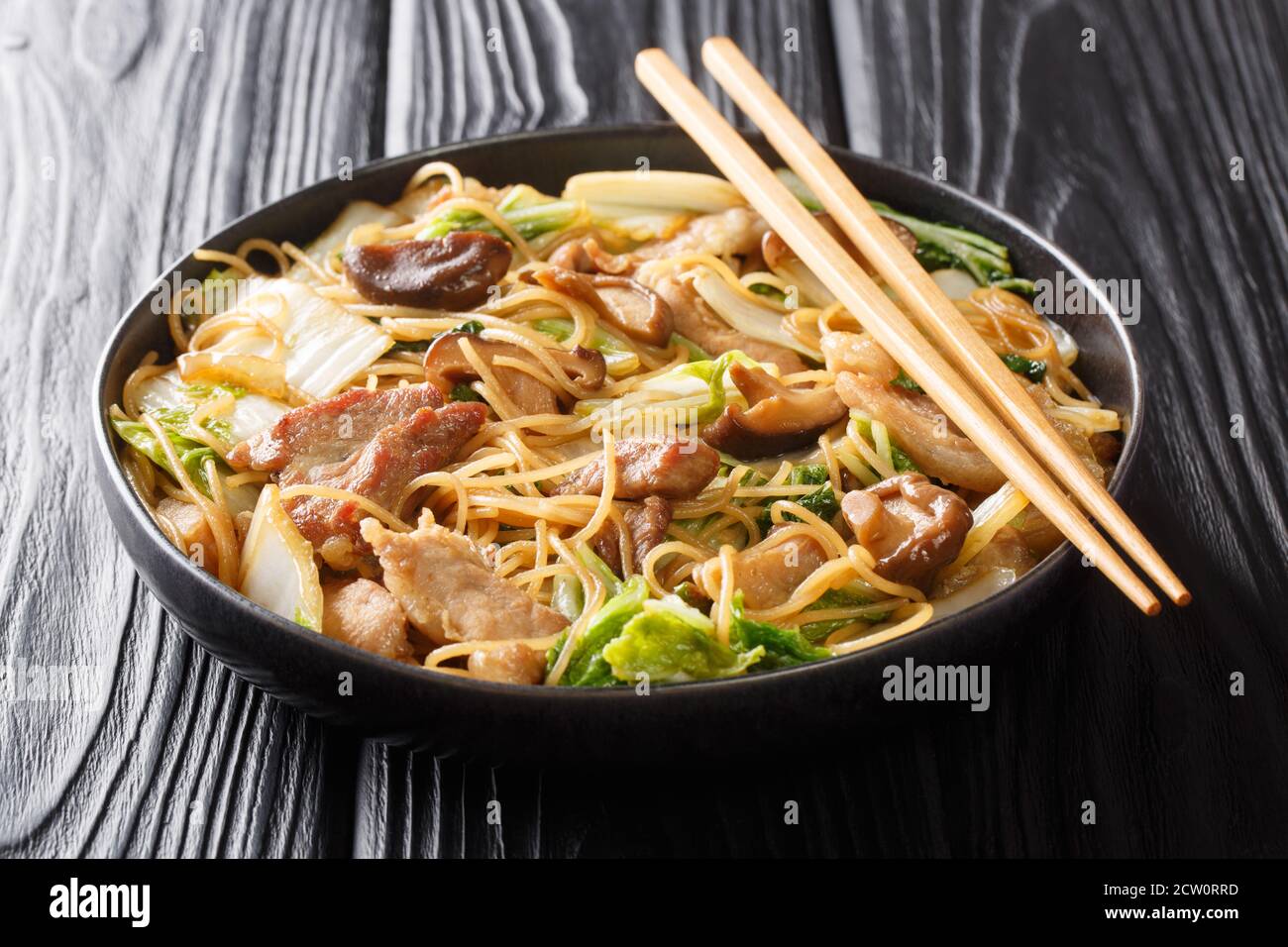 Leckere Cellophannudeln mit gebratenem Schweinebauch, Shiitake und napa-Kohl in Sojasauce close-up in einem Teller auf dem Tisch. Horizontal Stockfoto