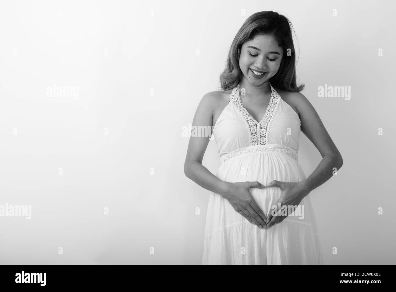 Glücklich junge asiatische schwangere Frau lächeln, während die Hand Herz unterzeichnen Sie auf ihrem Bauch mit Liebe für ihr Baby Stockfoto