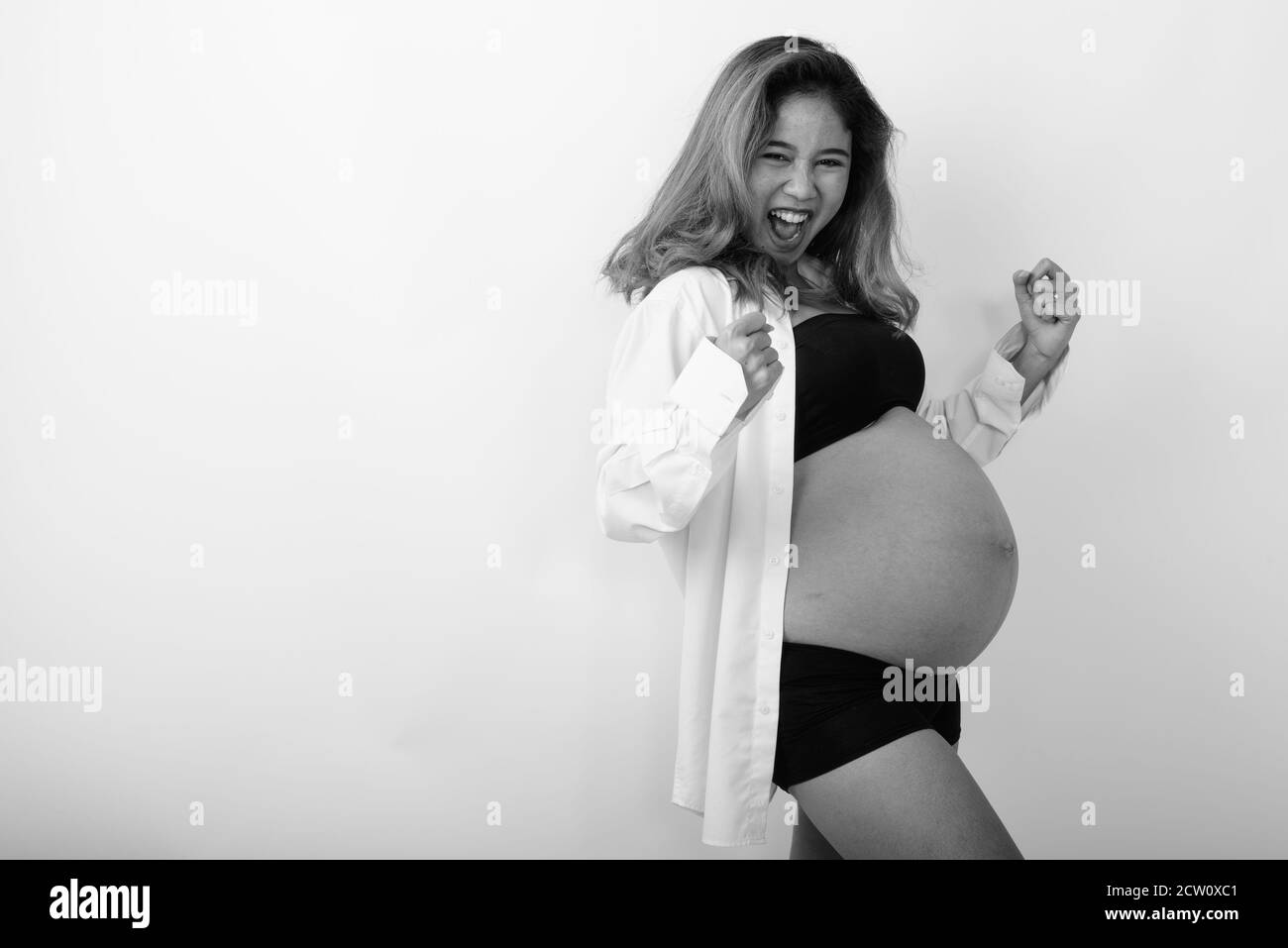 Studio Aufnahme von jungen glücklich asiatische schwangere Frau lächeln während Motiviertes Aussehen und offenes weißes Hemd Stockfoto
