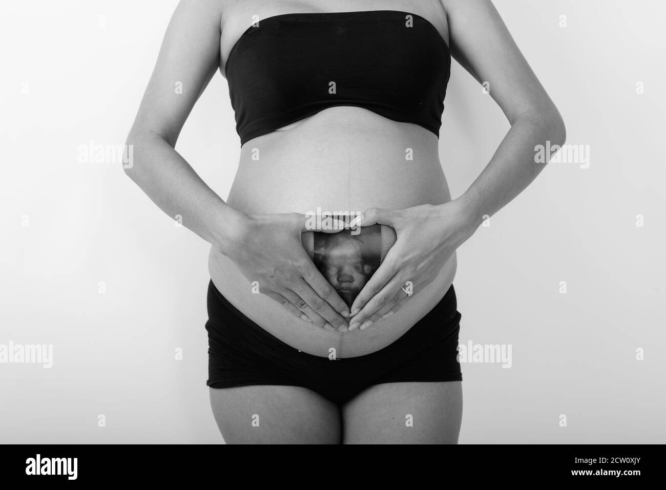 Junge asiatische schwangere Frau hält Sonogramm ihres Babys während Hand Herz Zeichen machen Stockfoto