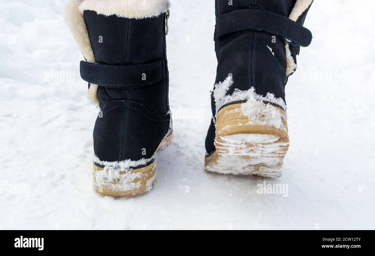 Weibliche Füße in schwarzen Stiefeln, die im Winterschnee entlang laufen Stockfoto
