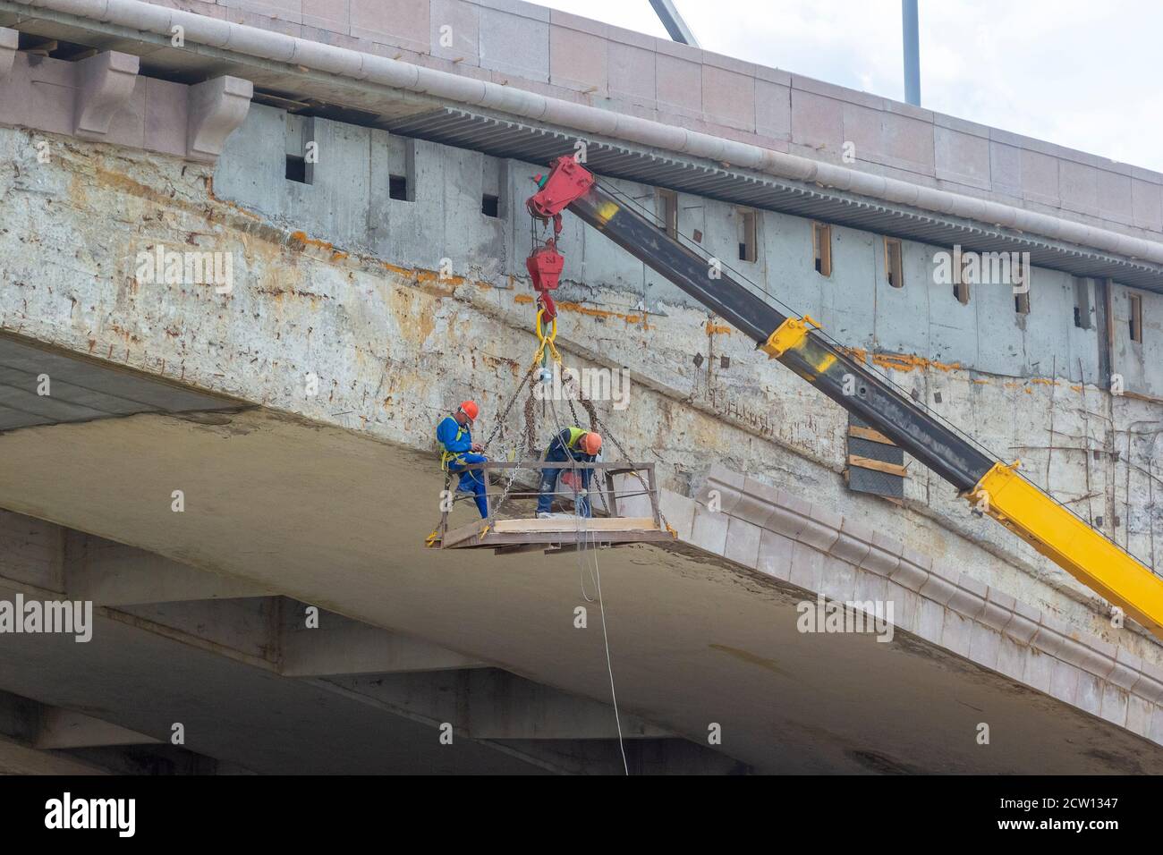 Männliche Arbeiter hängen und tun Reparaturarbeiten für eine Brücke Stockfoto