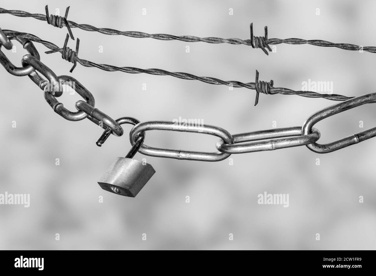Vorhängeschloss und Stahlketten mit Stacheldraht gegen bewölkten Himmel Symbol für Lockdown in Schwarzweiß Stockfoto